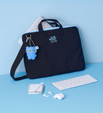 Black laptop bag with blue plush toy, white keyboard, and earbuds on a light blue background